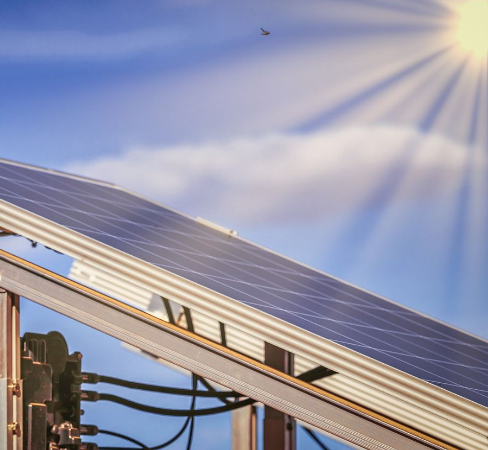 Close-up of a solar panel with visible electrical wiring on the left side. The panel is angled towards the sky, capturing bright sunlight, and there is a small bird flying above, reinforcing a scene of sustainability—an inspiring snapshot for those considering financing a solar system.